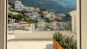 A view through an arched doorway of a balcony overlooking a hillside town with buildings and mountains in the background. - Hotel Posa Posa (Positano)