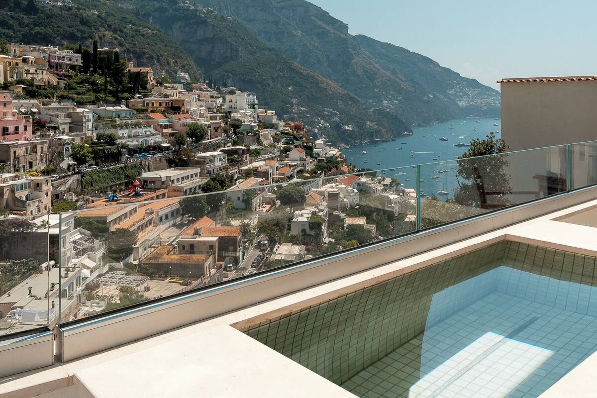 A poolside view with a clear view of a coastal town and mountains.