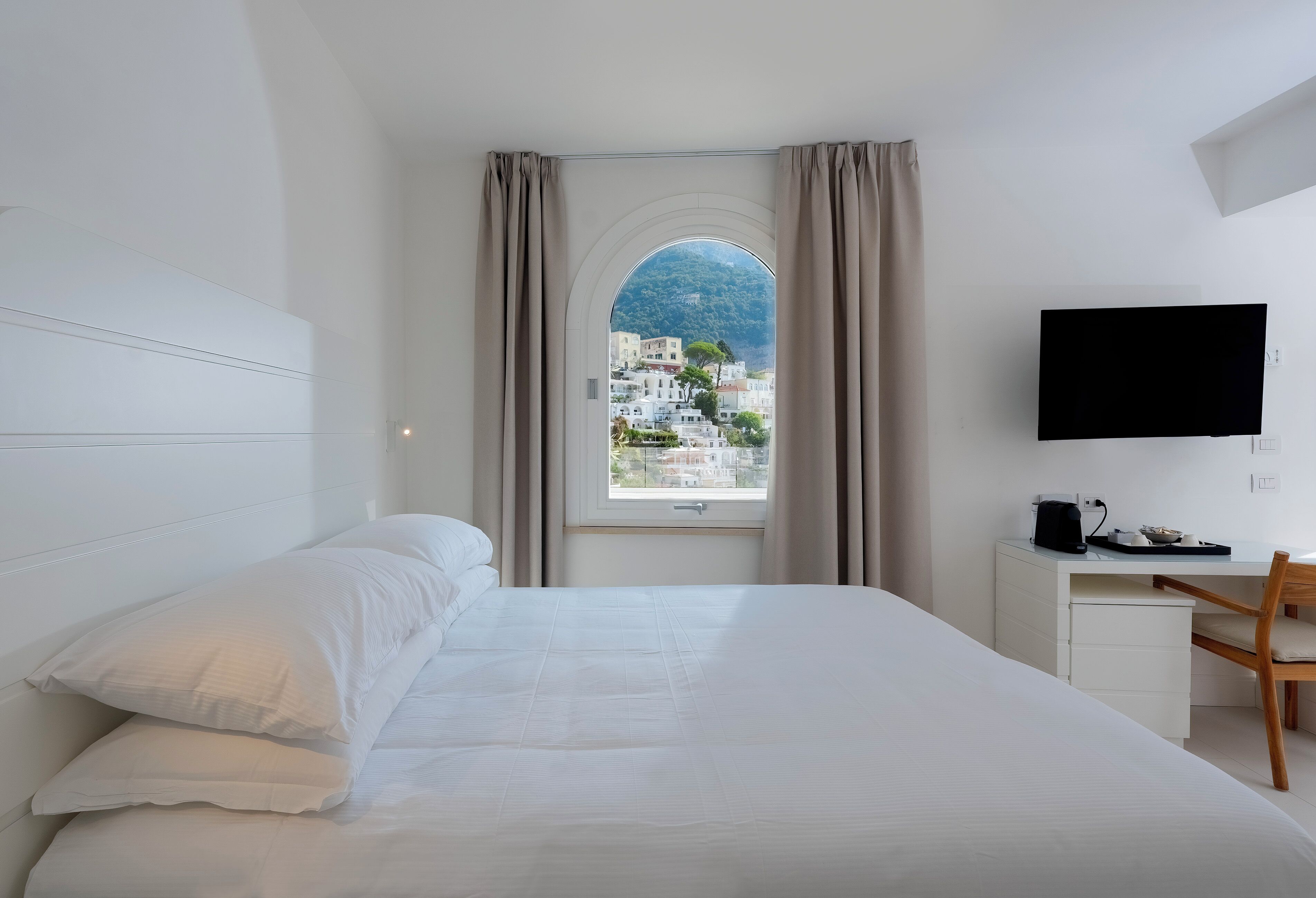 A hotel room with a bed, a desk, a chair, a TV, and a window with curtains.