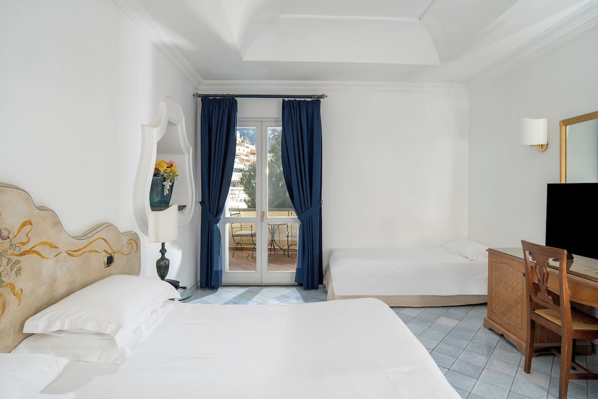 A hotel room with a bed, a desk, a chair, a TV, and a view of the outdoors through a glass door.