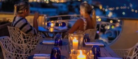 A dining table with candles, blue glasses, and white chairs.