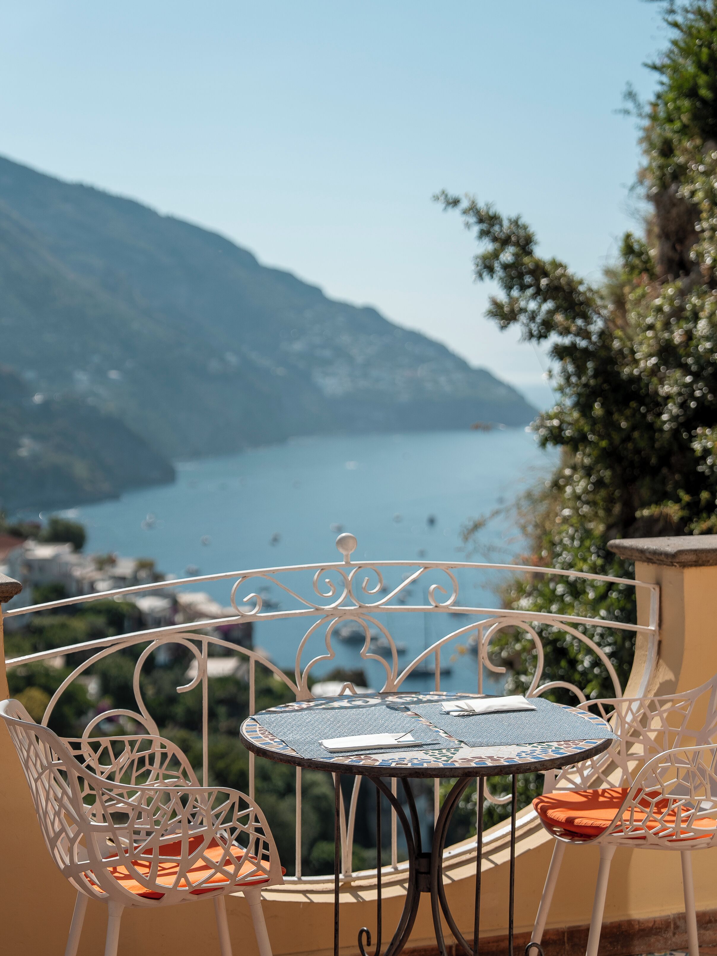 A balcony with a table and chairs overlooking a lake and mountains.