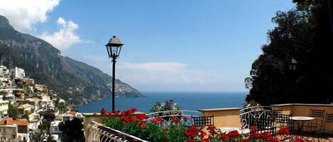 A coastal town with a balcony overlooking the sea, featuring a street lamp and red flowers.