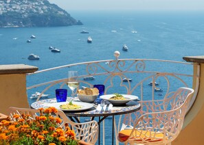 A table with plates of food, a glass of wine, and blue glasses on a balcony overlooking the sea with boats. - Hotel Posa Posa (Positano)
