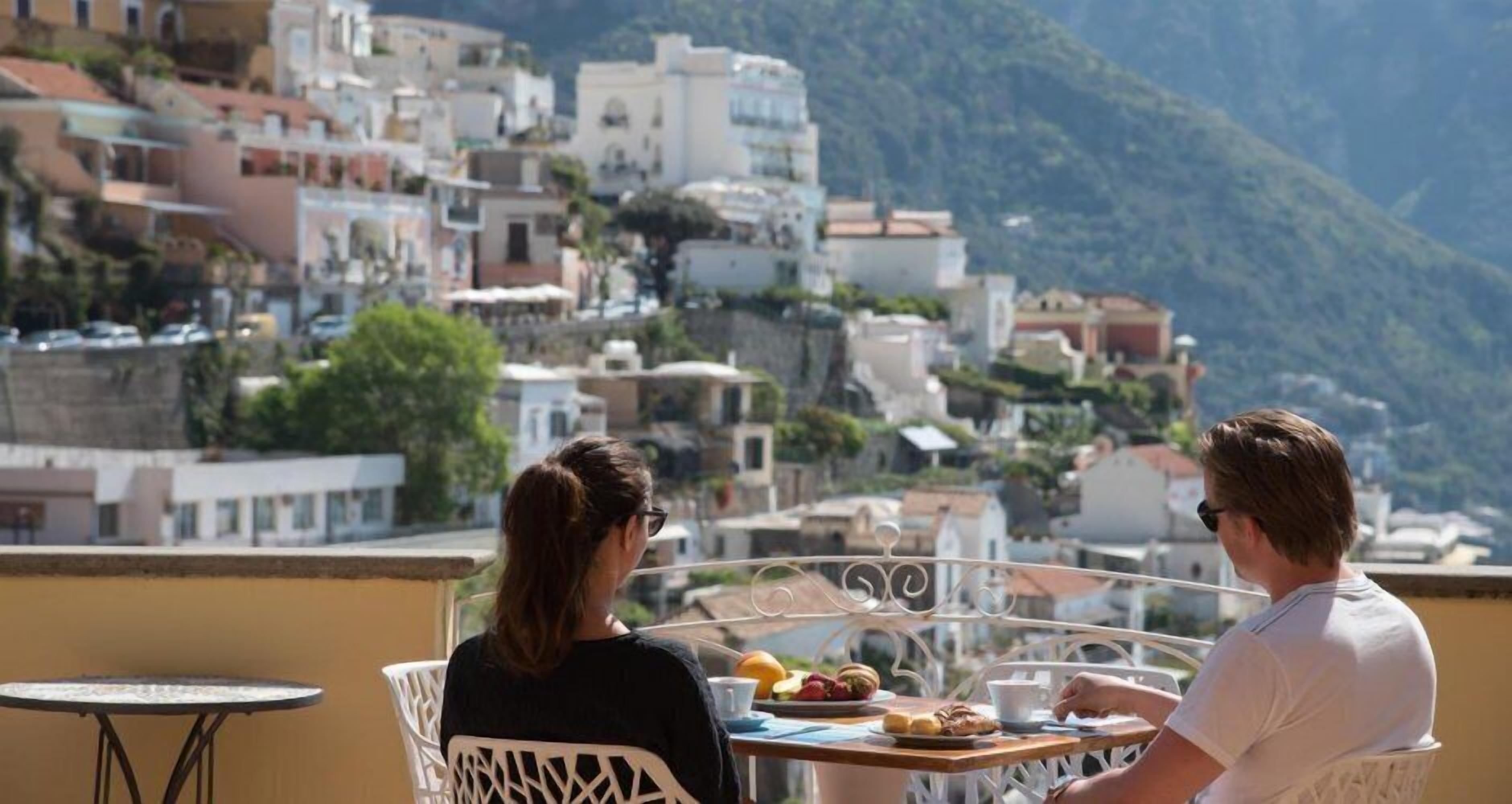 Une terrasse avec une table dressée pour deux personnes, donnant sur une colline parsemée de bâtiments.