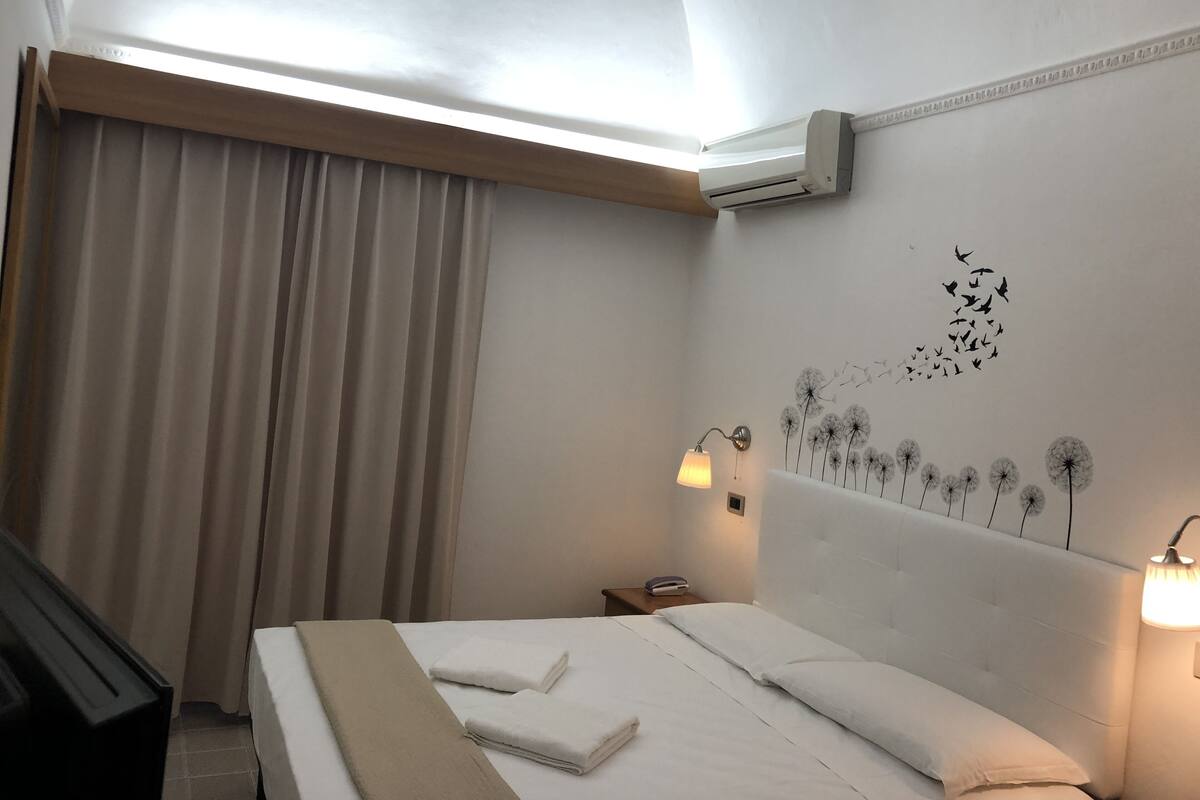 Une chambre d’hôtel avec un lit, une table de chevet, une lampe et une décoration murale représentant des pissenlits.