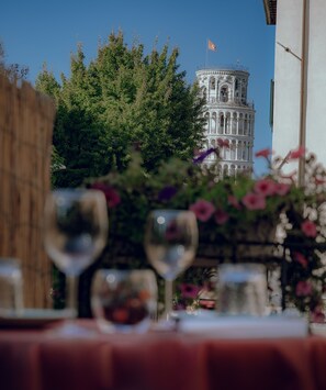 Uma mesa com copos de vinho e um arranjo de flores, com vista para uma torre histórica ao fundo.
