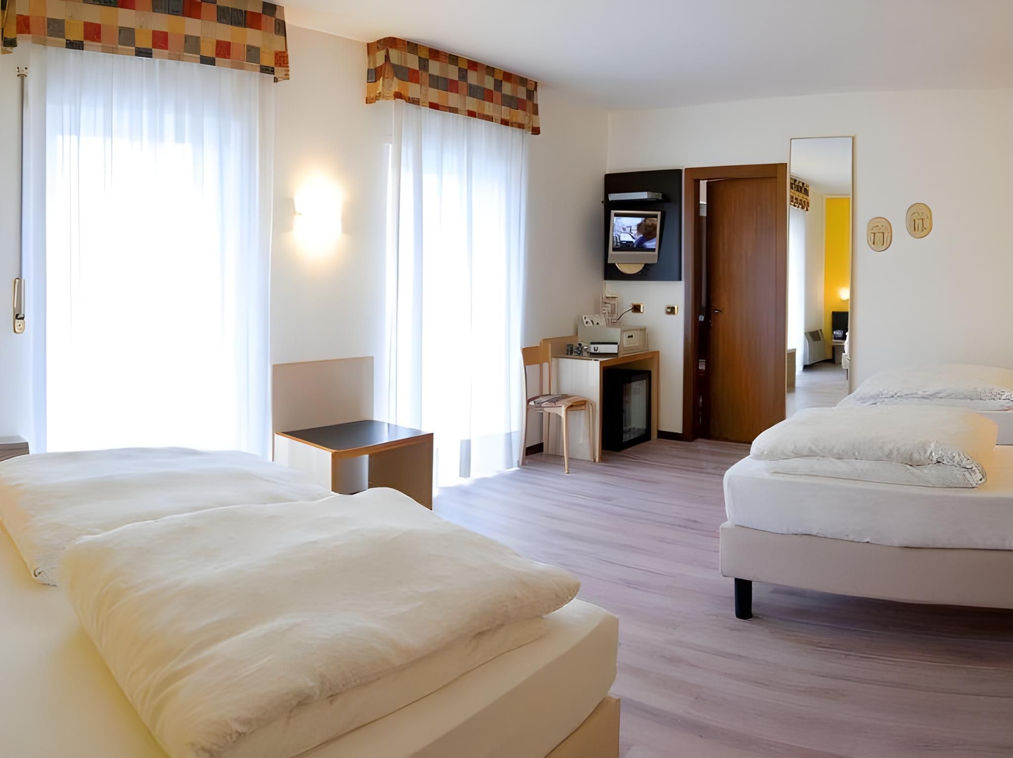 Une chambre d’hôtel avec deux lits, un bureau, une chaise, une télévision et un miroir.