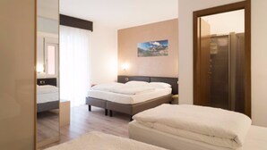 Une chambre d’hôtel avec un lit, une table de chevet, un miroir, un tableau accroché au mur et une porte.