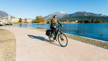 Une personne à vélo, circulant sur une piste cyclable le long du bord de l’eau, avec des bâtiments et des montagnes en arrière-plan.