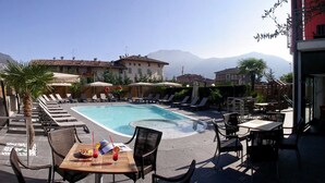 Un espace piscine avec des chaises longues, une table avec des boissons et une vue sur les bâtiments et les montagnes.