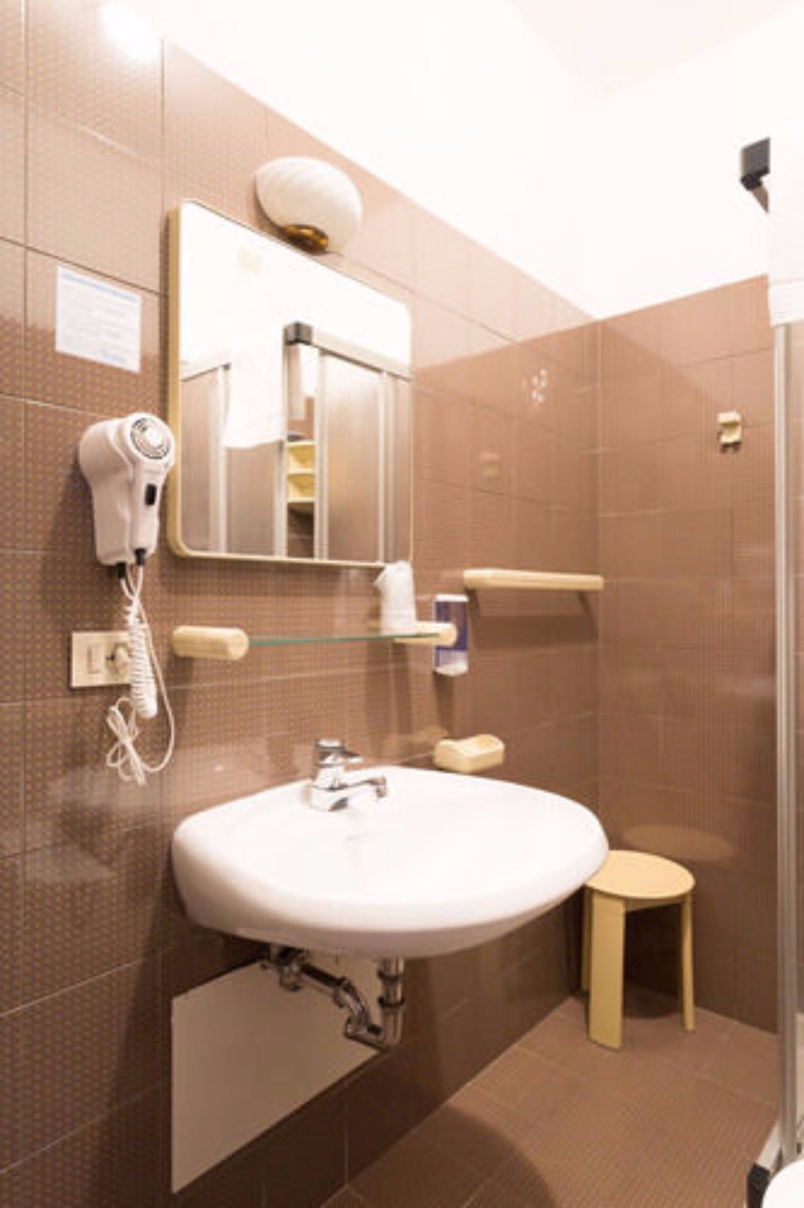 Ein Badezimmer mit Waschbecken, Spiegel, Föhn und einem kleinen Hocker.