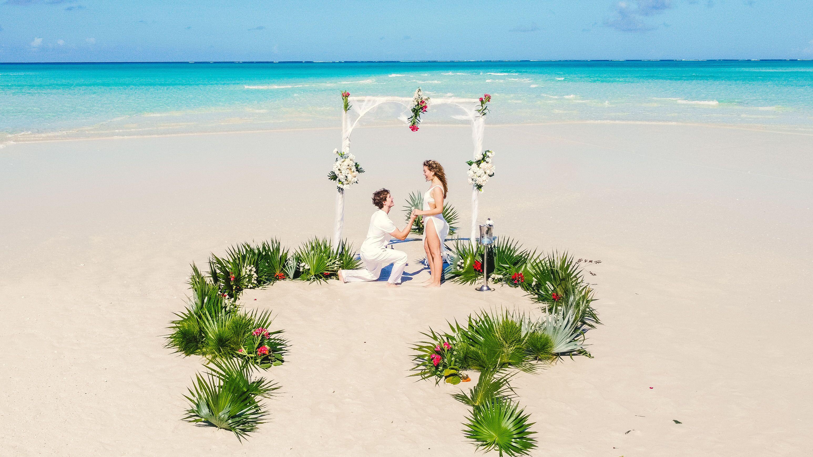 Une cérémonie de mariage organisée sur la plage, avec une décoration florale en forme de cœur et une arche blanche.