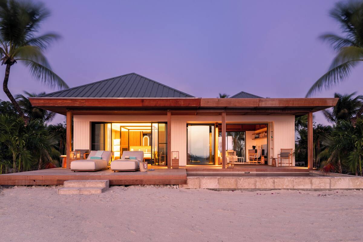 A modern beachfront house with a spacious living area, a visible kitchen, and a large glass door leading to the interior.