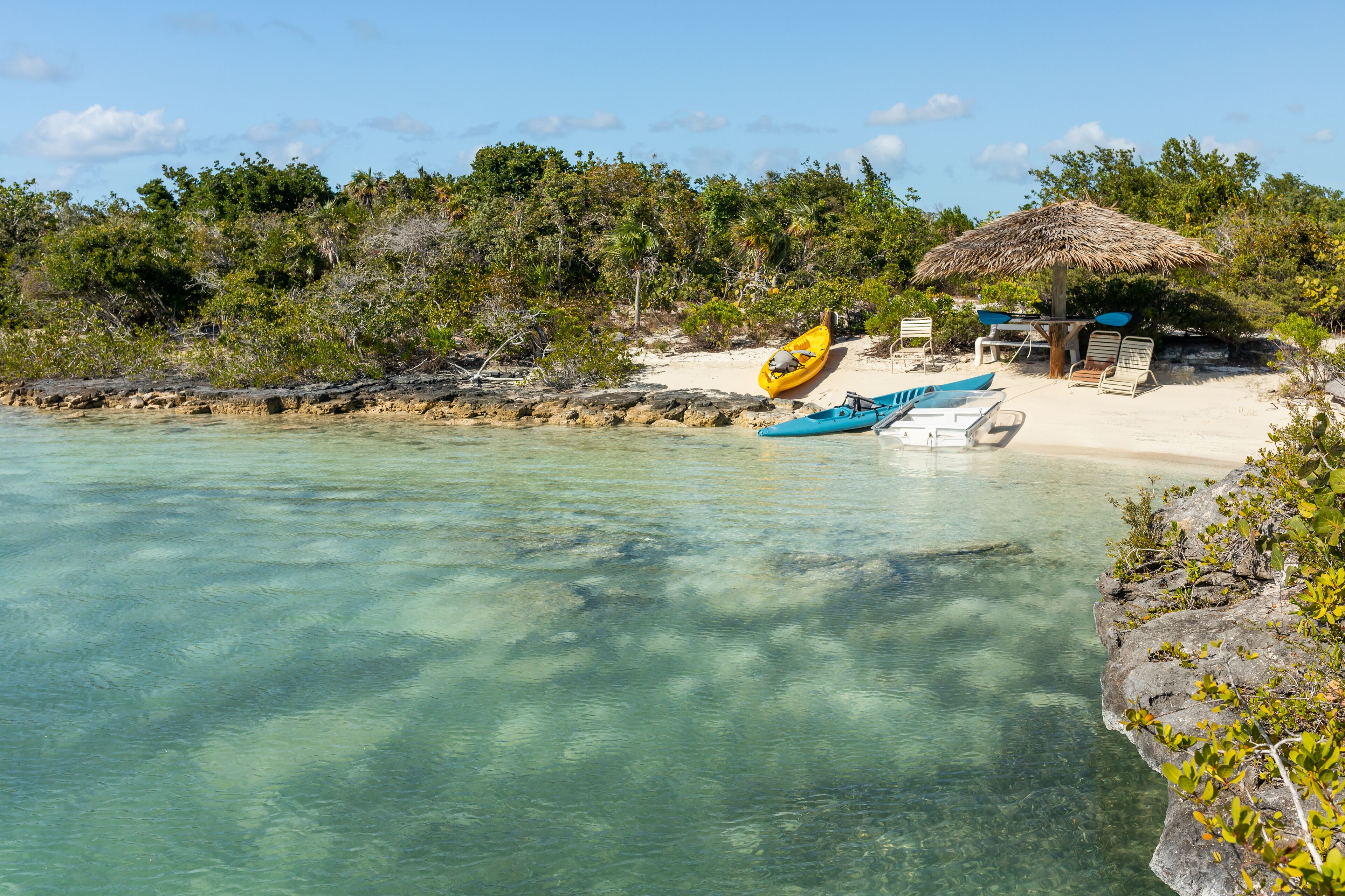 Una playa con agua turquesa cristalina, una cabaña con techo de paja y kayaks.