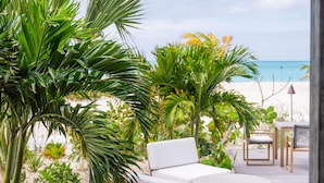 A wooden deck with a wicker lounge chair and ottoman, surrounded by tropical plants and overlooking a beach. - Pine Cay, Turks and Caicos (Pine Cay)