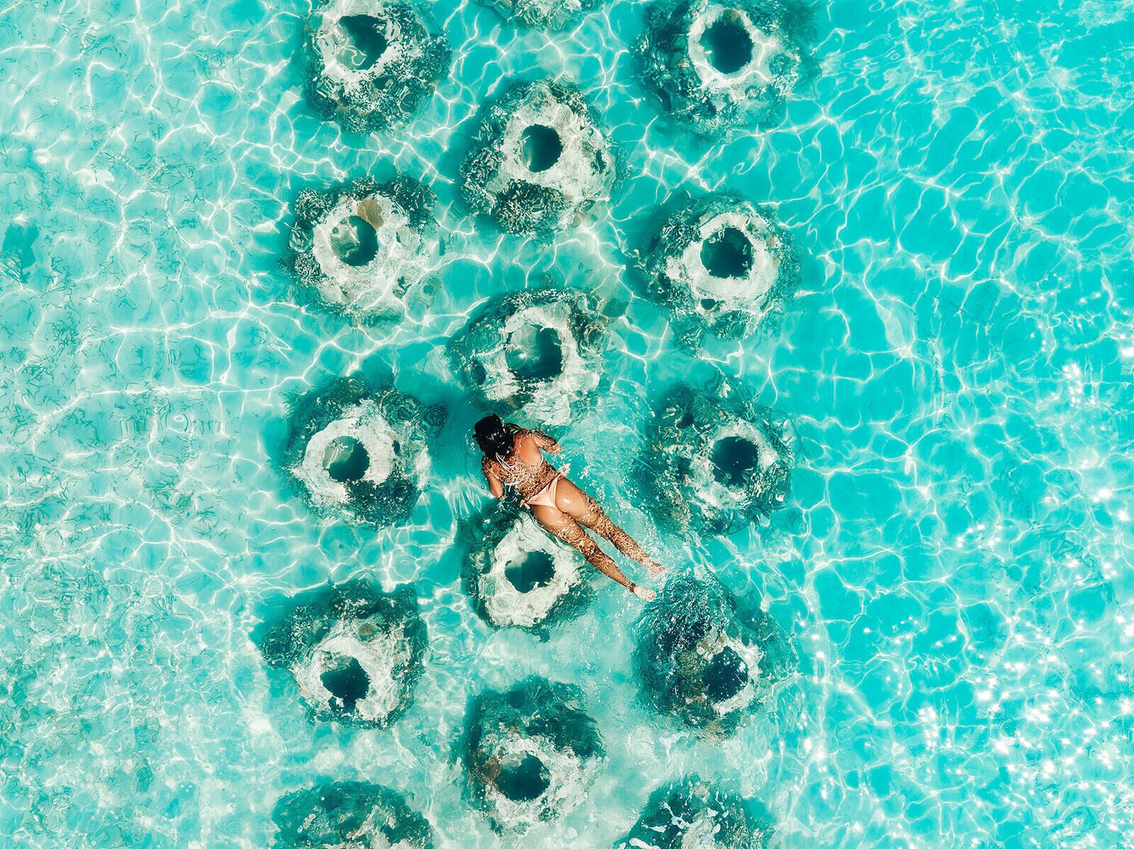 Una piscina turquesa cristalina con formaciones circulares y una persona nadando.