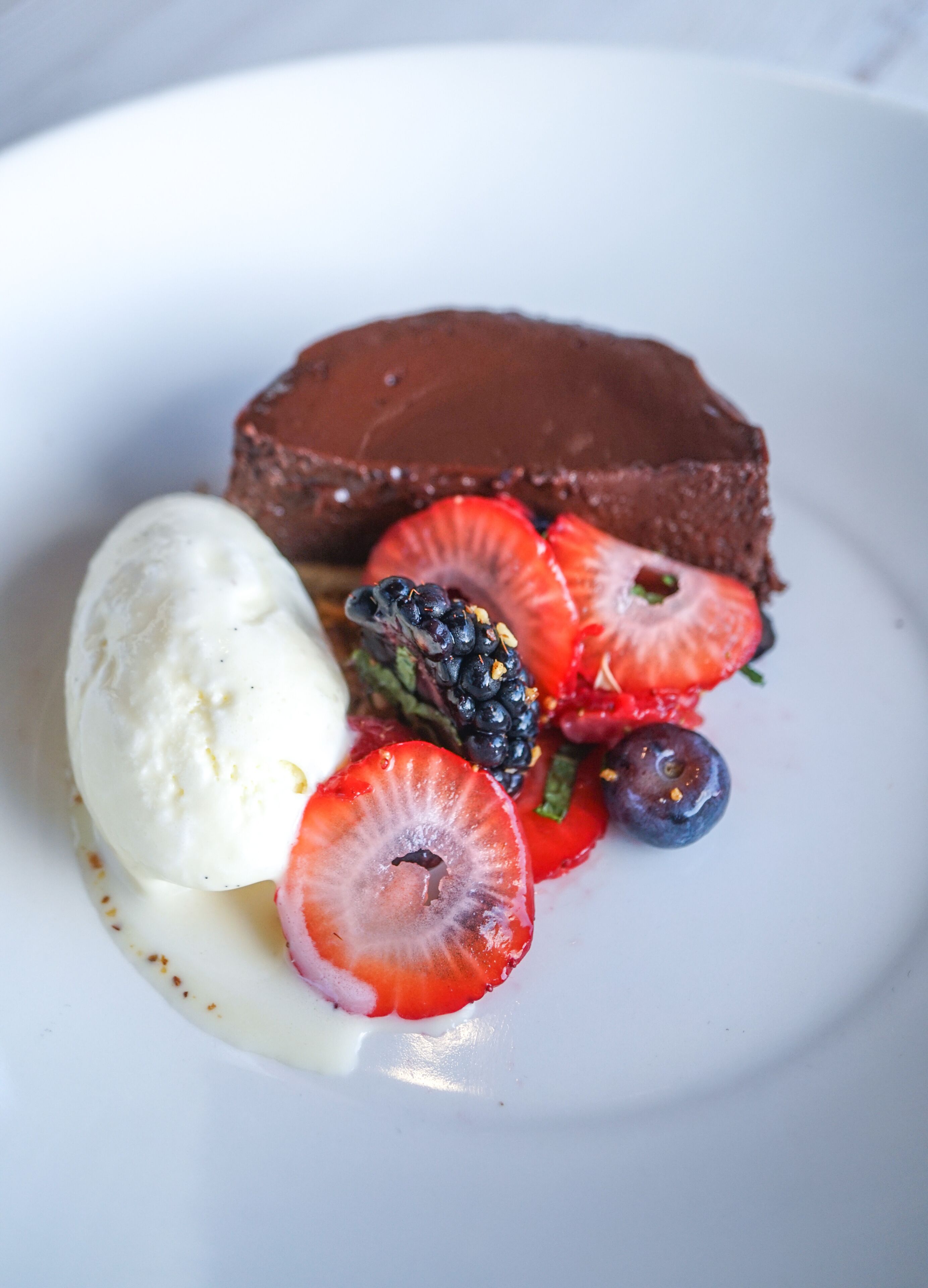 Um prato de sobremesa com bolo de chocolate, uma bola de sorvete de baunilha e frutas vermelhas frescas.