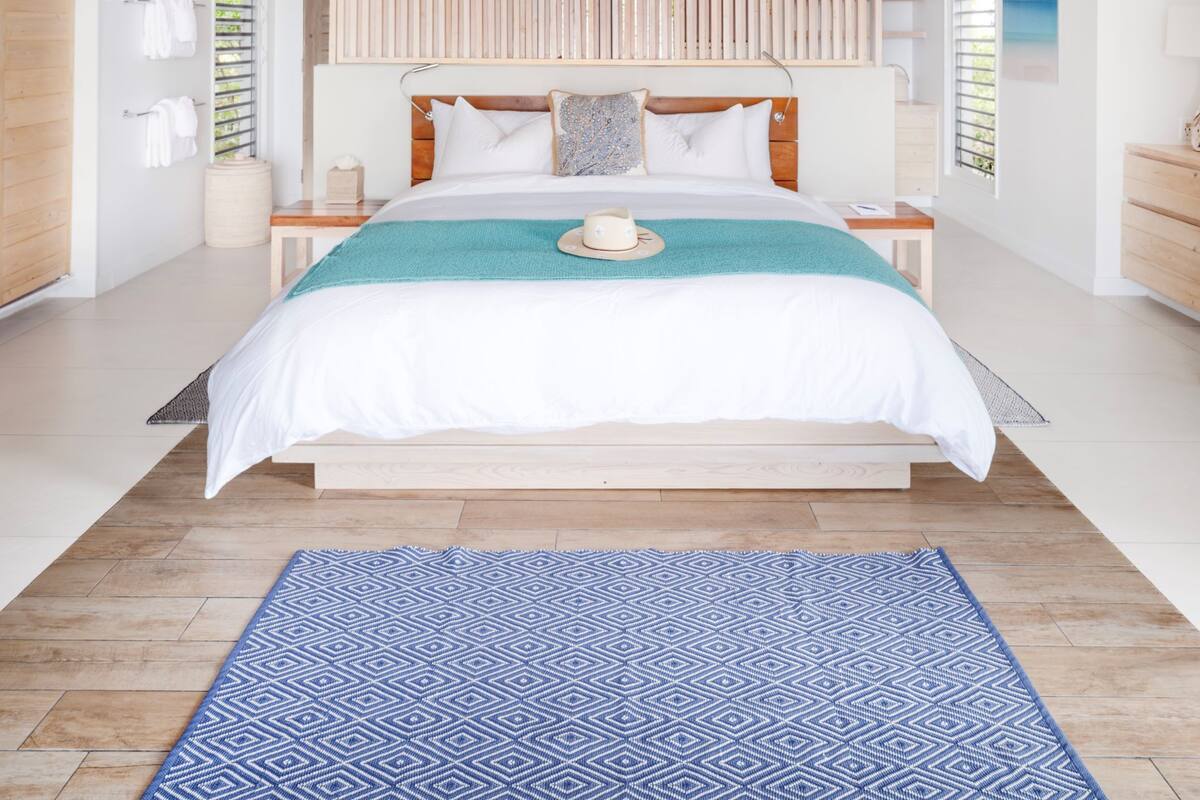 A modern bedroom with a large bed, wooden slats, a ceiling fan, and a view of the outdoors.