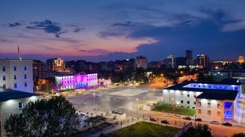 Paisatge urbà al capvespre, amb edificis il·luminats i una gran plaça oberta.