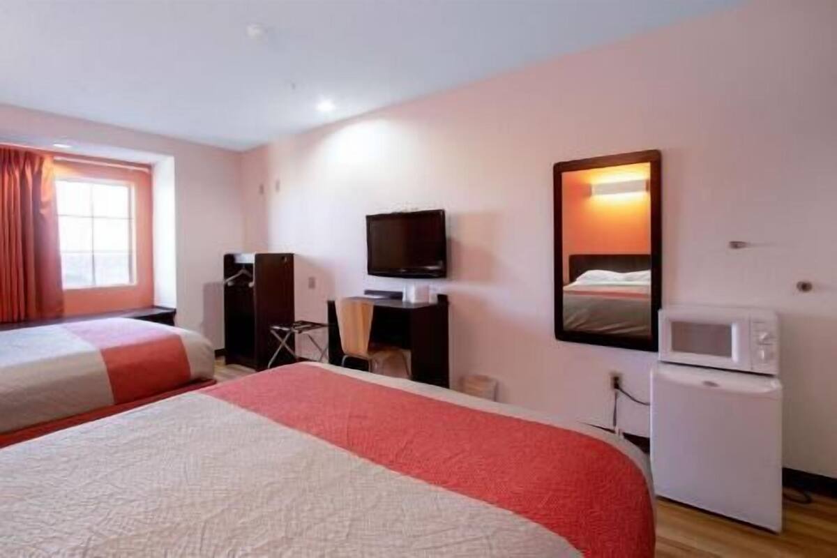 A hotel room with two beds, a television, a small desk, and a microwave.