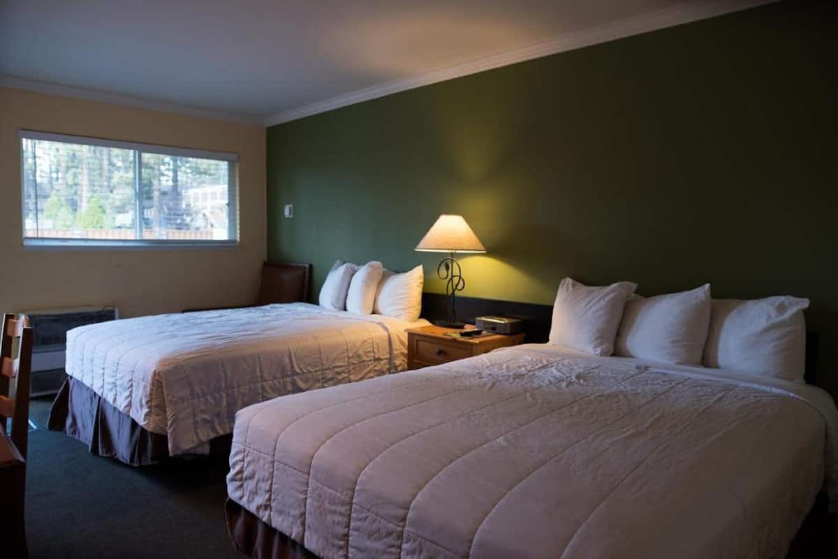 Une chambre d’hôtel avec deux lits, une table de chevet avec une lampe, une fenêtre donnant sur des arbres et une chaise.
