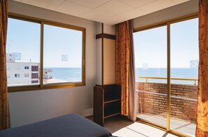 Una habitación con cama, un pequeño armario de madera y un balcón con barandilla.