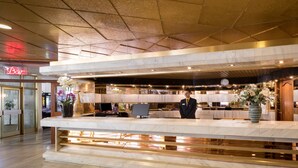 Zona de recepción de hotel con mostrador de mármol, un reloj y un cartel que dice 'Bar'.