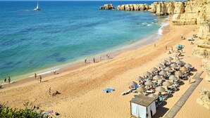 A beach with clear blue water, rocky cliffs, and a sandy shore with umbrellas and beach chairs. - Hotel Baia Grande (Albufeira)