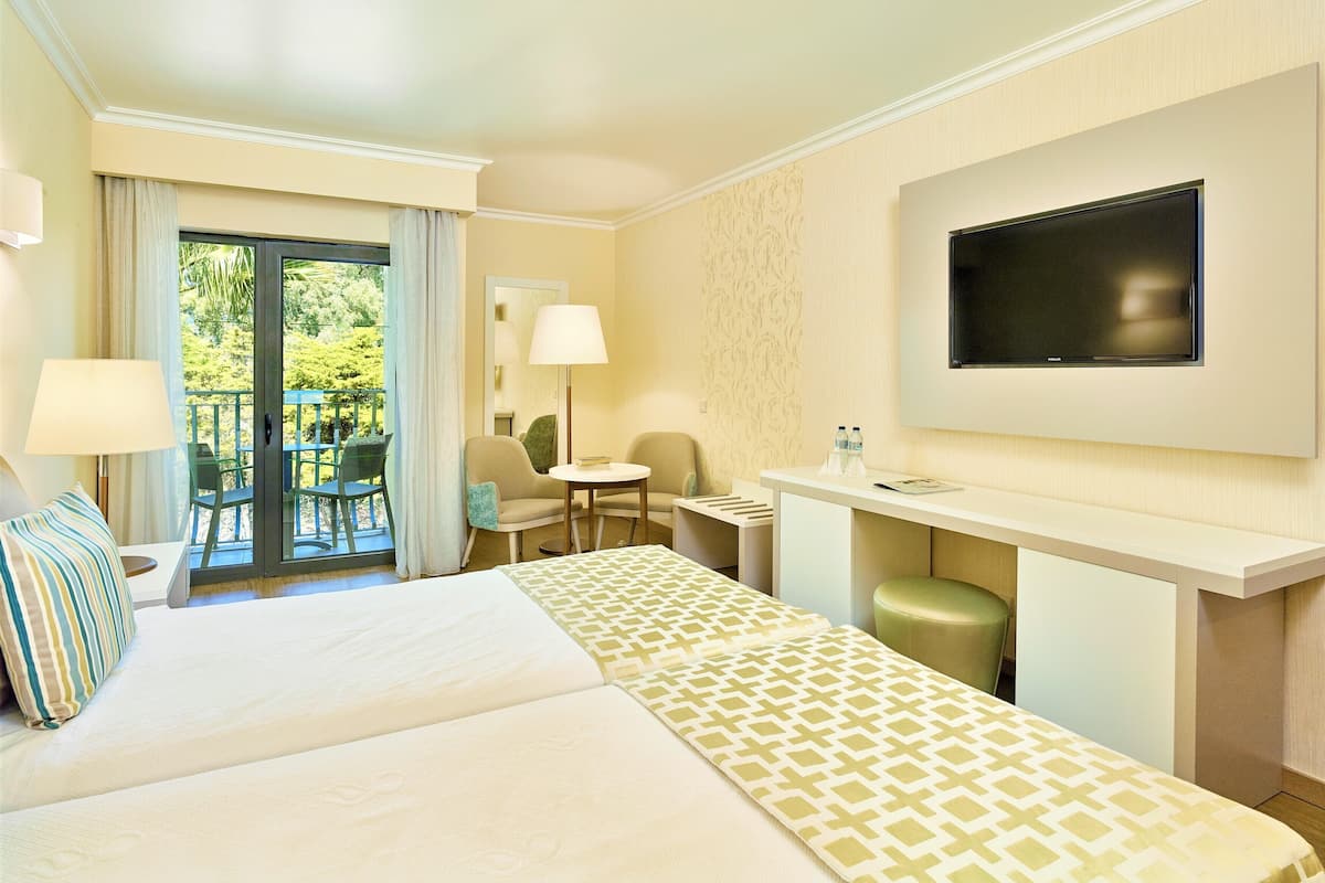 A hotel room with a bed, a desk, a chair, a TV, and a balcony with outdoor seating.