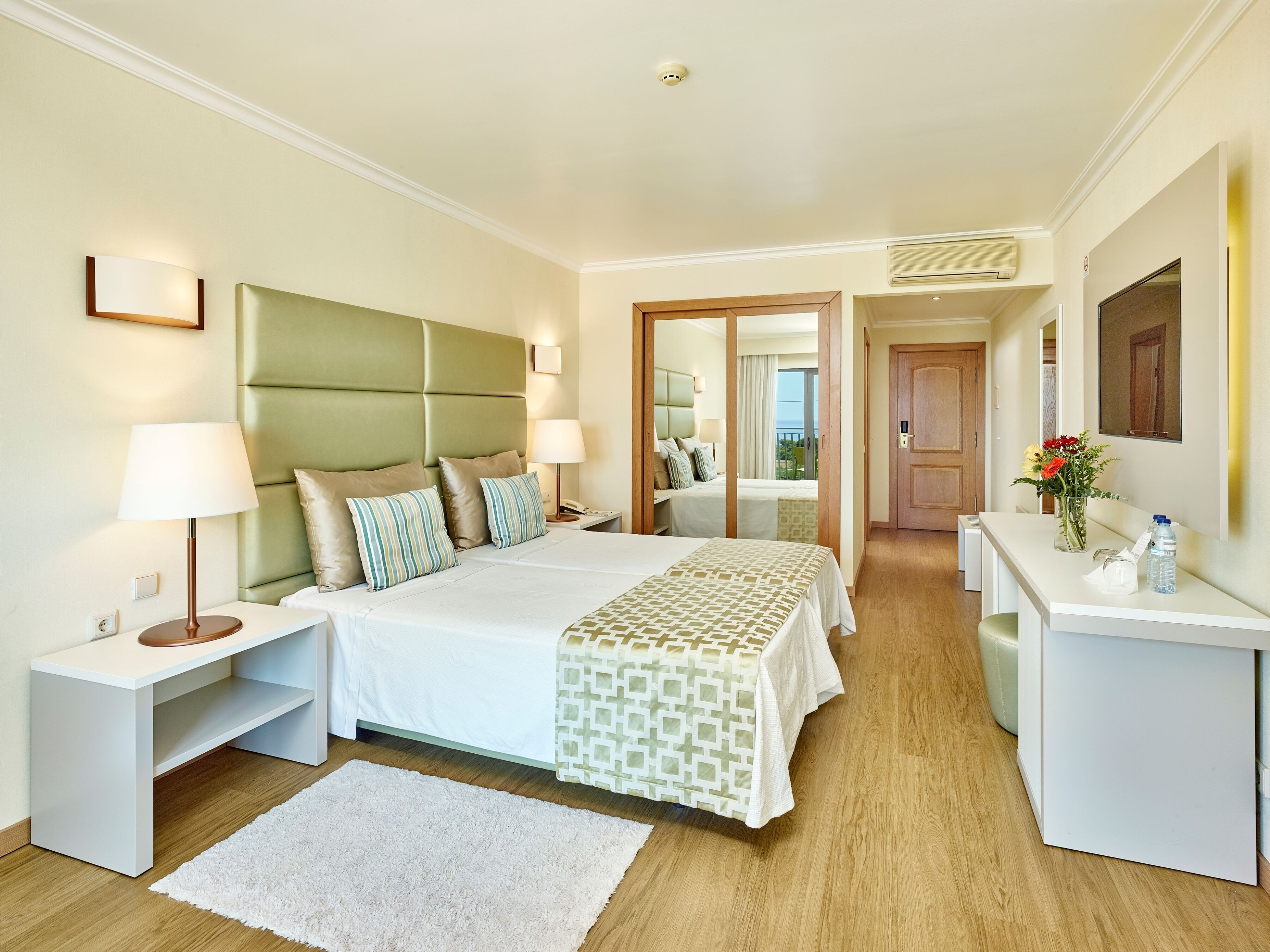 A hotel room with a large bed, bedside tables, a desk, a mirror, and a view of the outdoors.