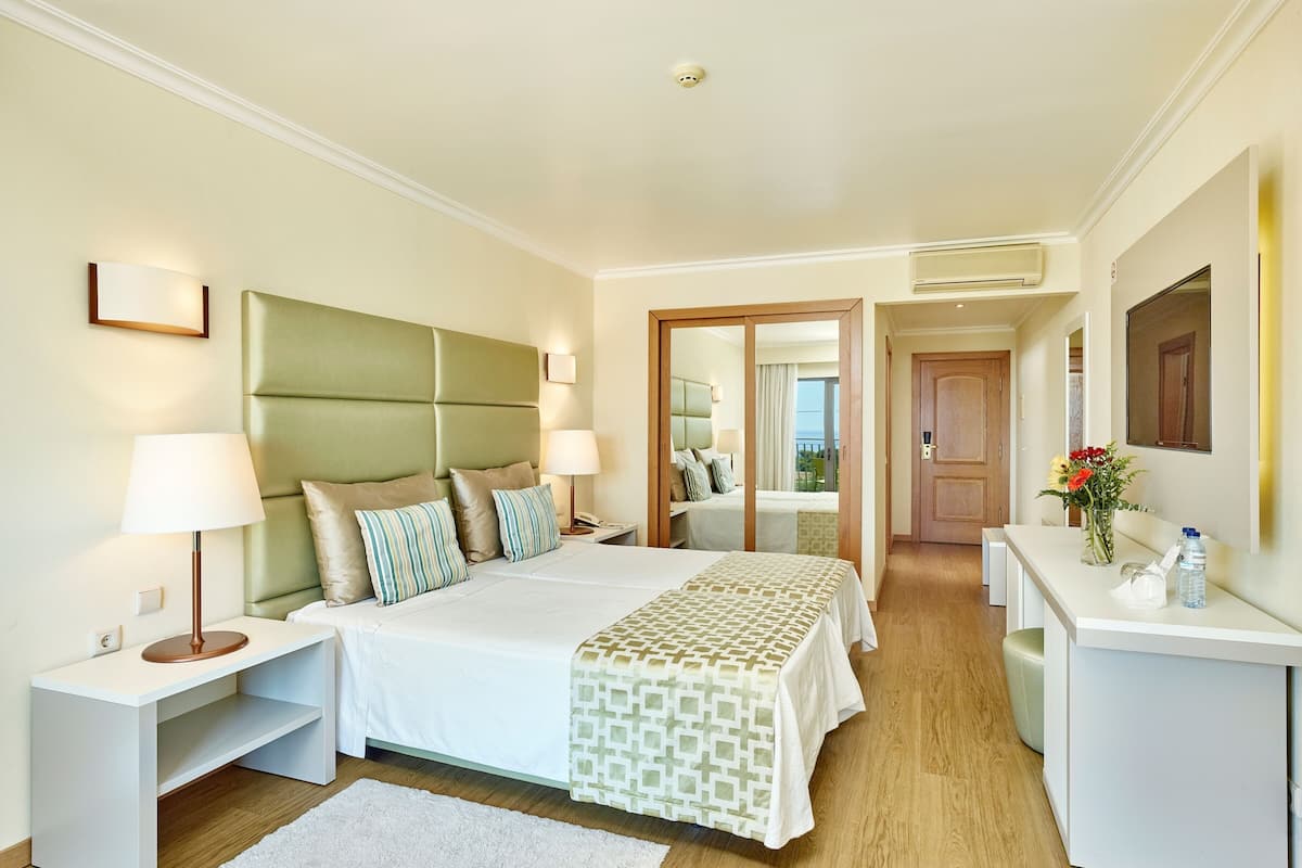 A hotel room with a large bed, bedside tables, a desk, a mirror, and a view of the outdoors.