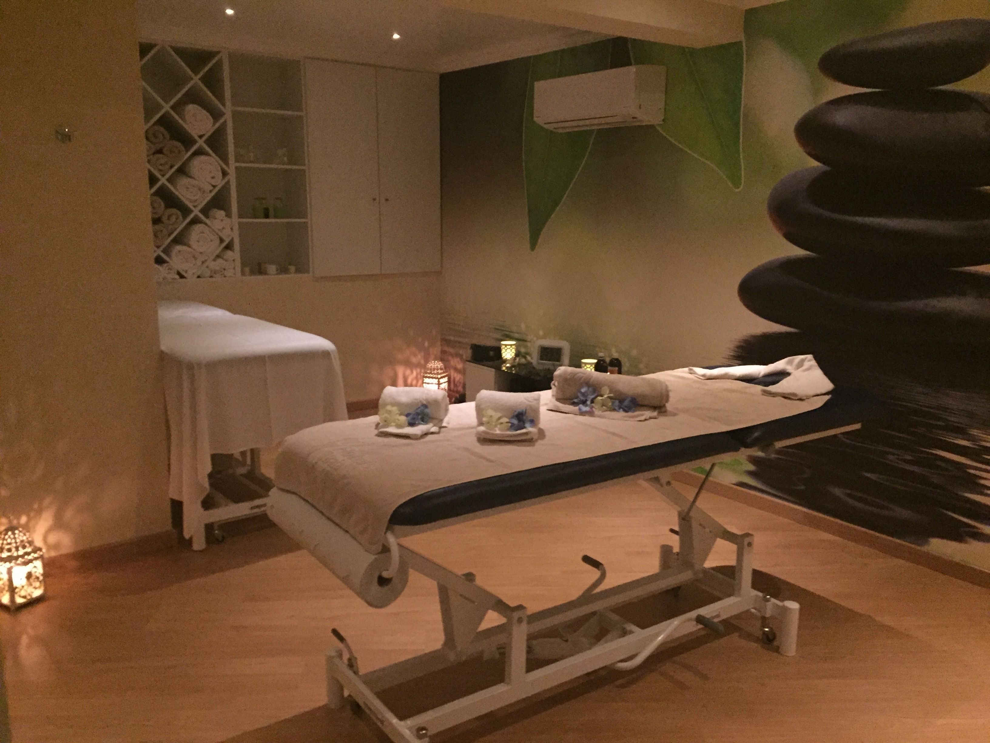 Ett rum för massagebehandlingar med en massagebänk, handdukar och en liten lampa.
