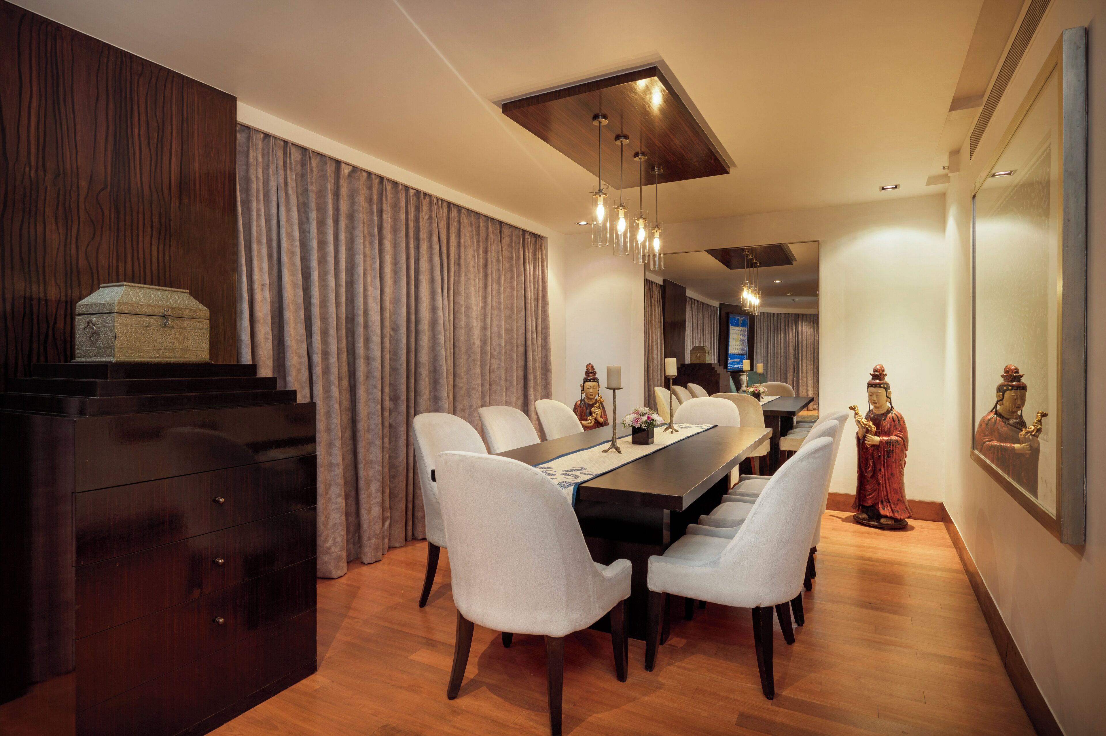 A dining area with a long table, white chairs, a wooden cabinet, and two statues.