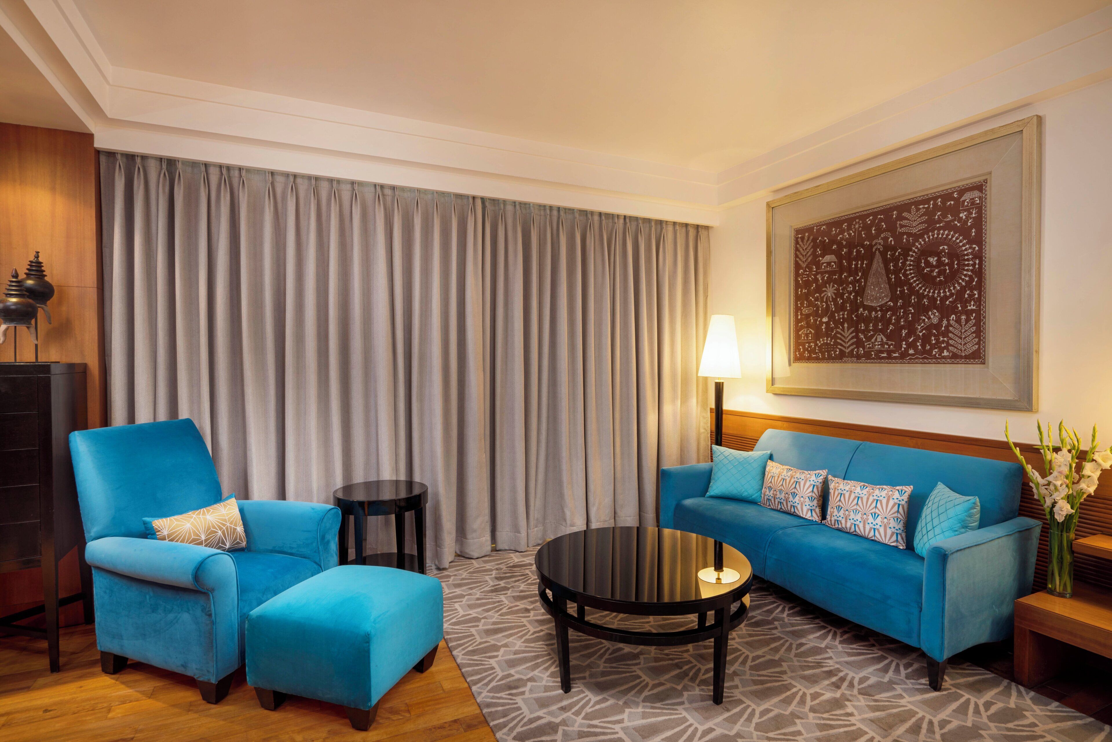 A hotel room with a blue sofa, a matching armchair, a small round table, and a large abstract painting on the wall.