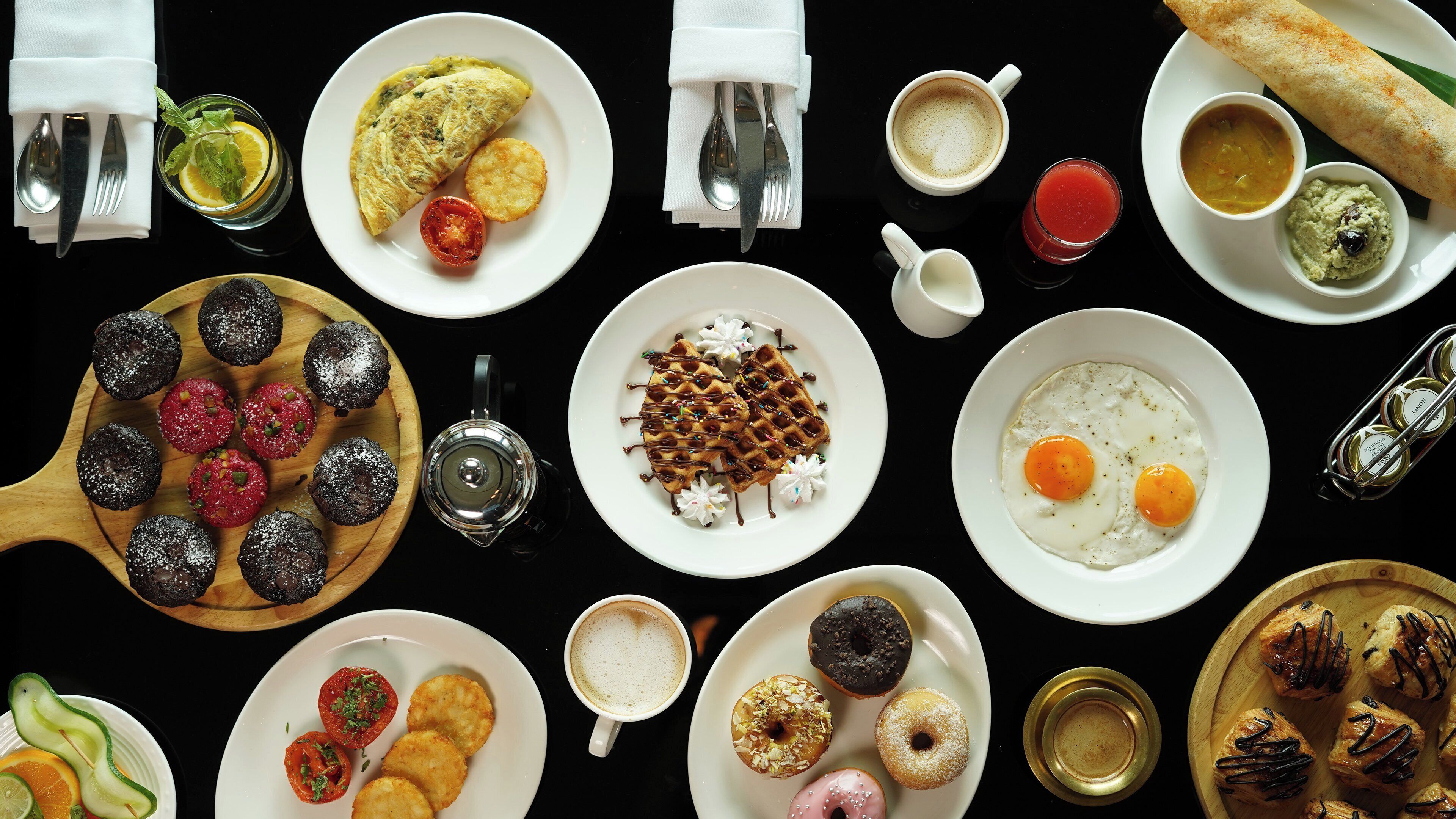 Diversos platos de desayuno, como waffles, huevos y pastelería, presentados en varias fuentes.