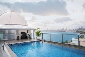 Piscina no terraço com vista para o horizonte urbano, área de estar coberta e uma grande estrutura em cúpula branca.