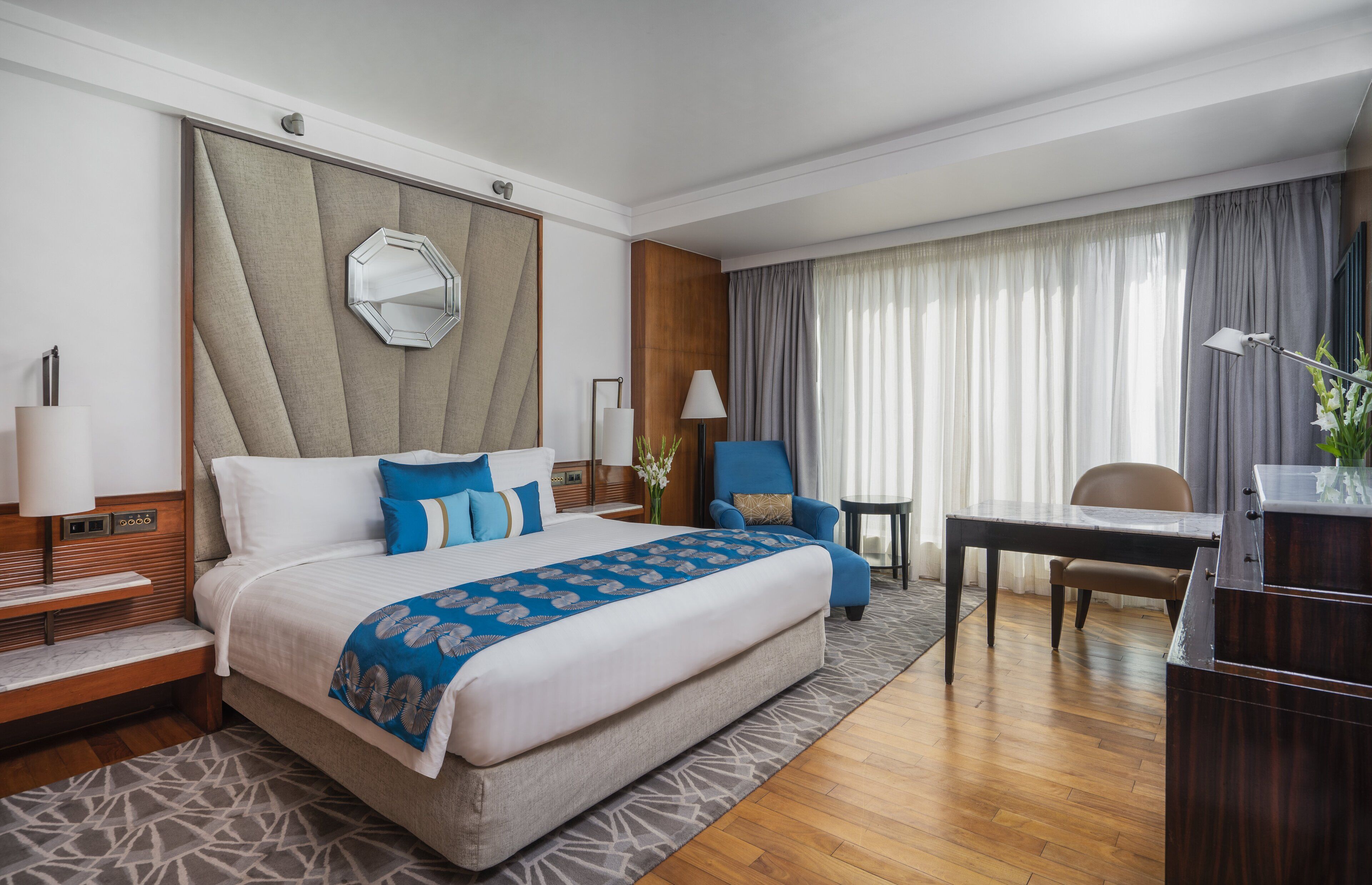 Une chambre d’hôtel avec un grand lit, un bureau, une chaise, une lampe et un miroir au mur.