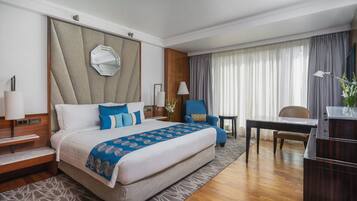 Une chambre d’hôtel avec un grand lit, un bureau, une chaise, une lampe et un miroir au mur.