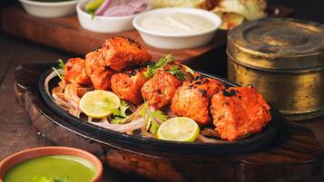 A plate of tandoori chicken with lemon slices and onions, accompanied by various sauces and a brass container.