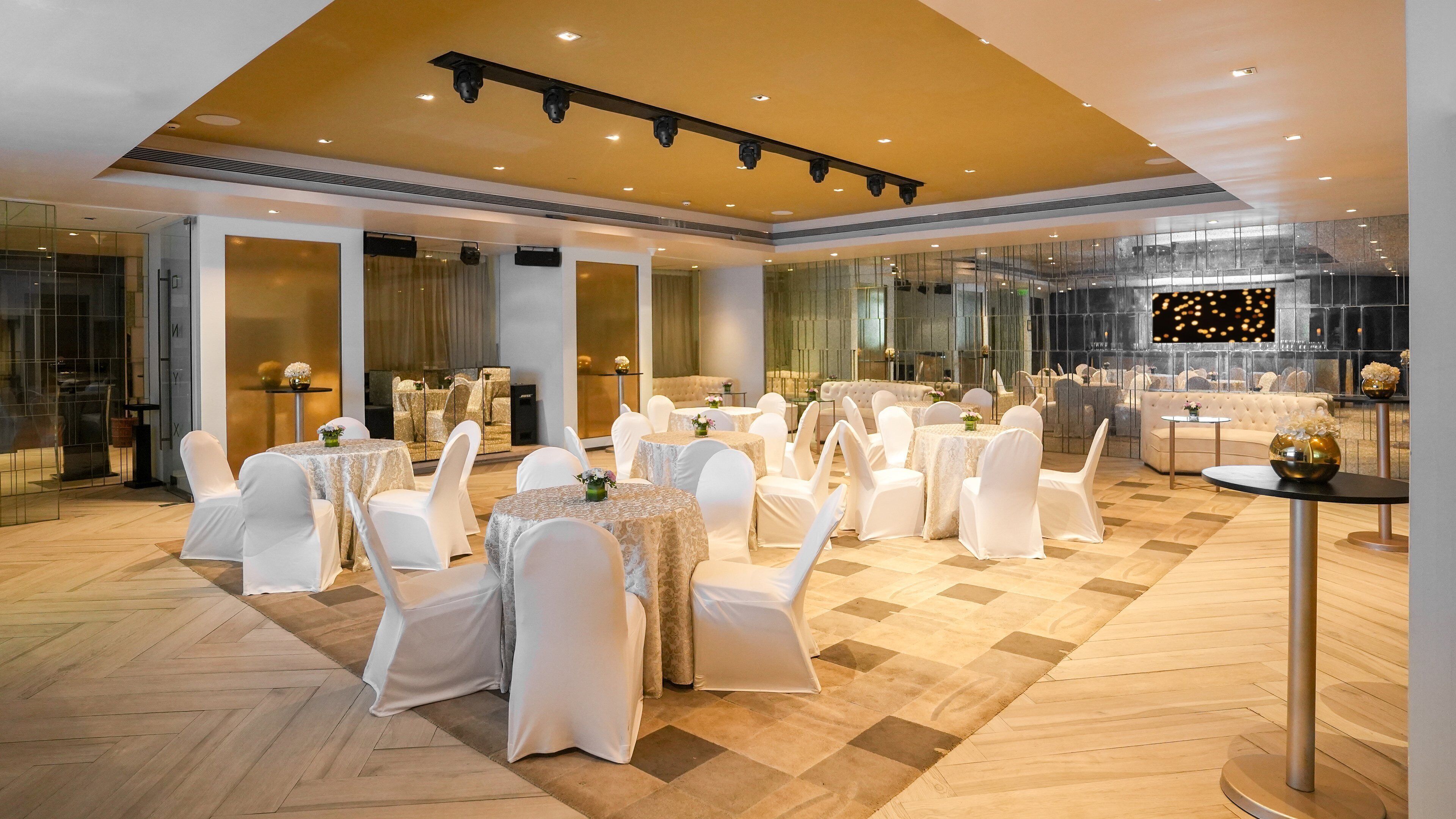 A spacious banquet hall with round tables and white chairs, large windows, and a modern ceiling design.