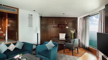 A modern hotel room with a sofa, armchairs, a desk, and a television.