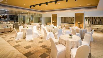 A spacious banquet hall with round tables and white chairs, a large seating area with sofas, and a modern interior design.