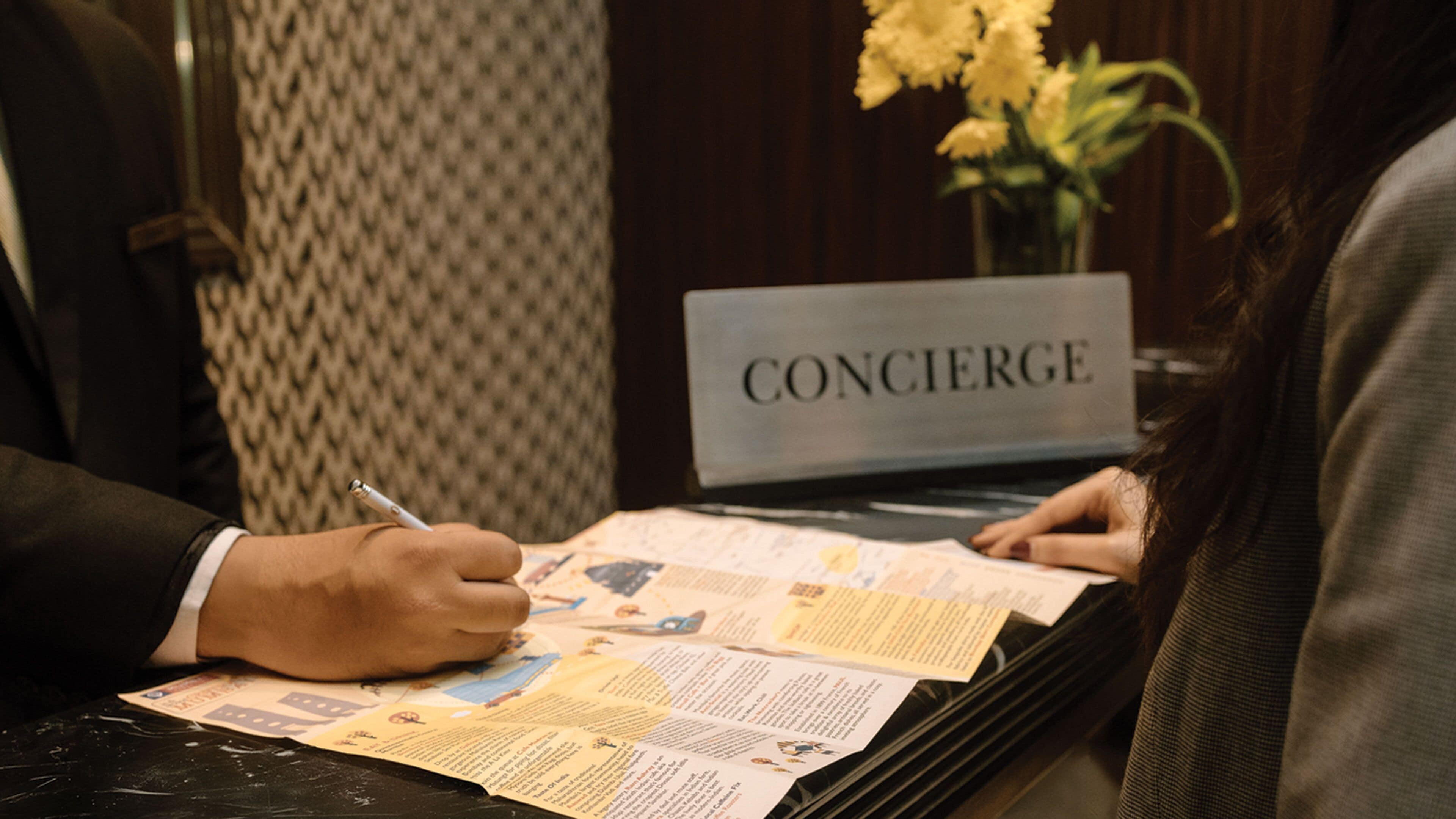 A concierge desk with a sign reading "CONCIERGE" and a person signing a document.