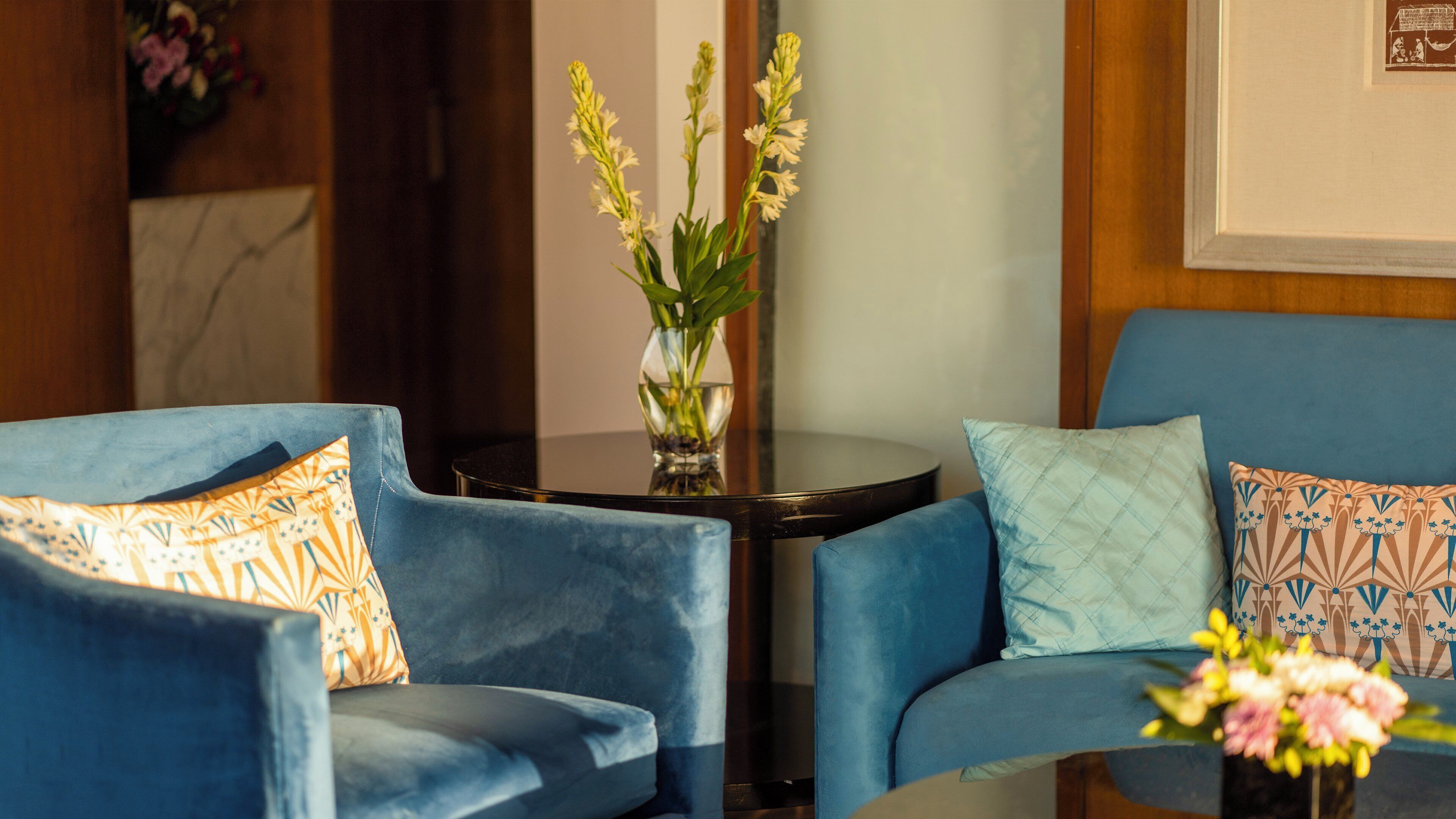 A room with two blue armchairs, a small round table, and a vase with flowers.