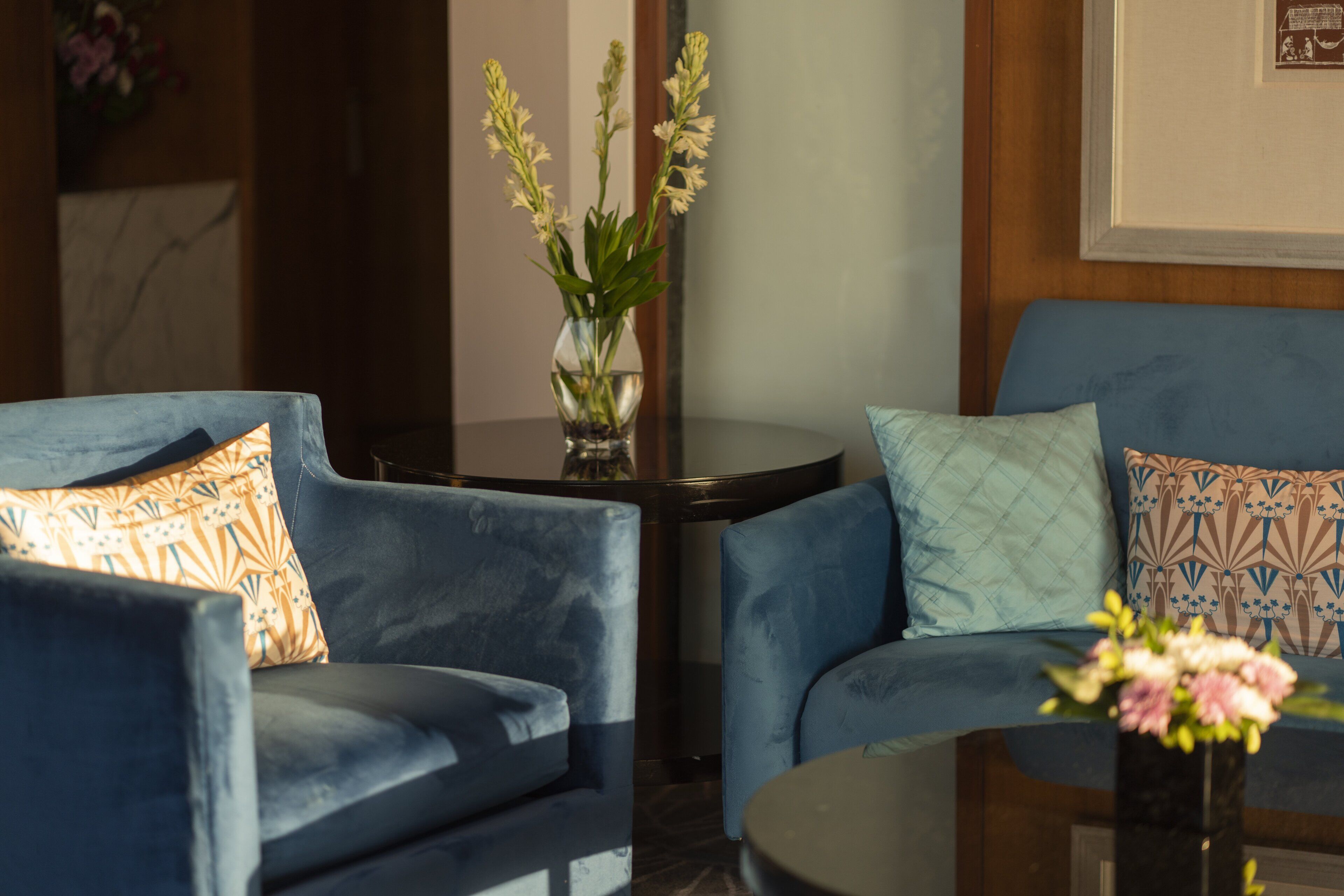A room with two blue armchairs, a small round table, and a vase with flowers.