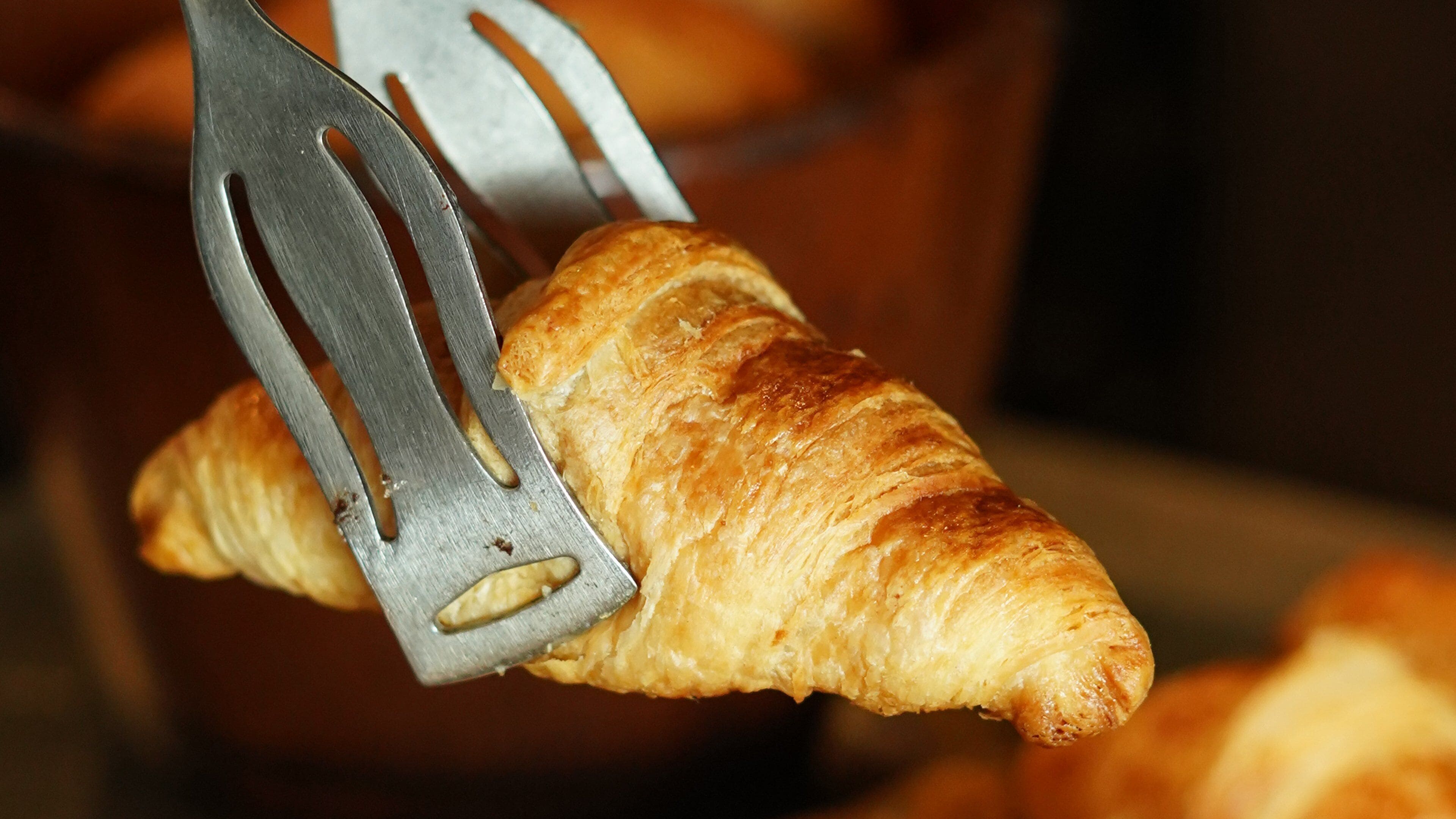 A croissant being held by a metal spatula.