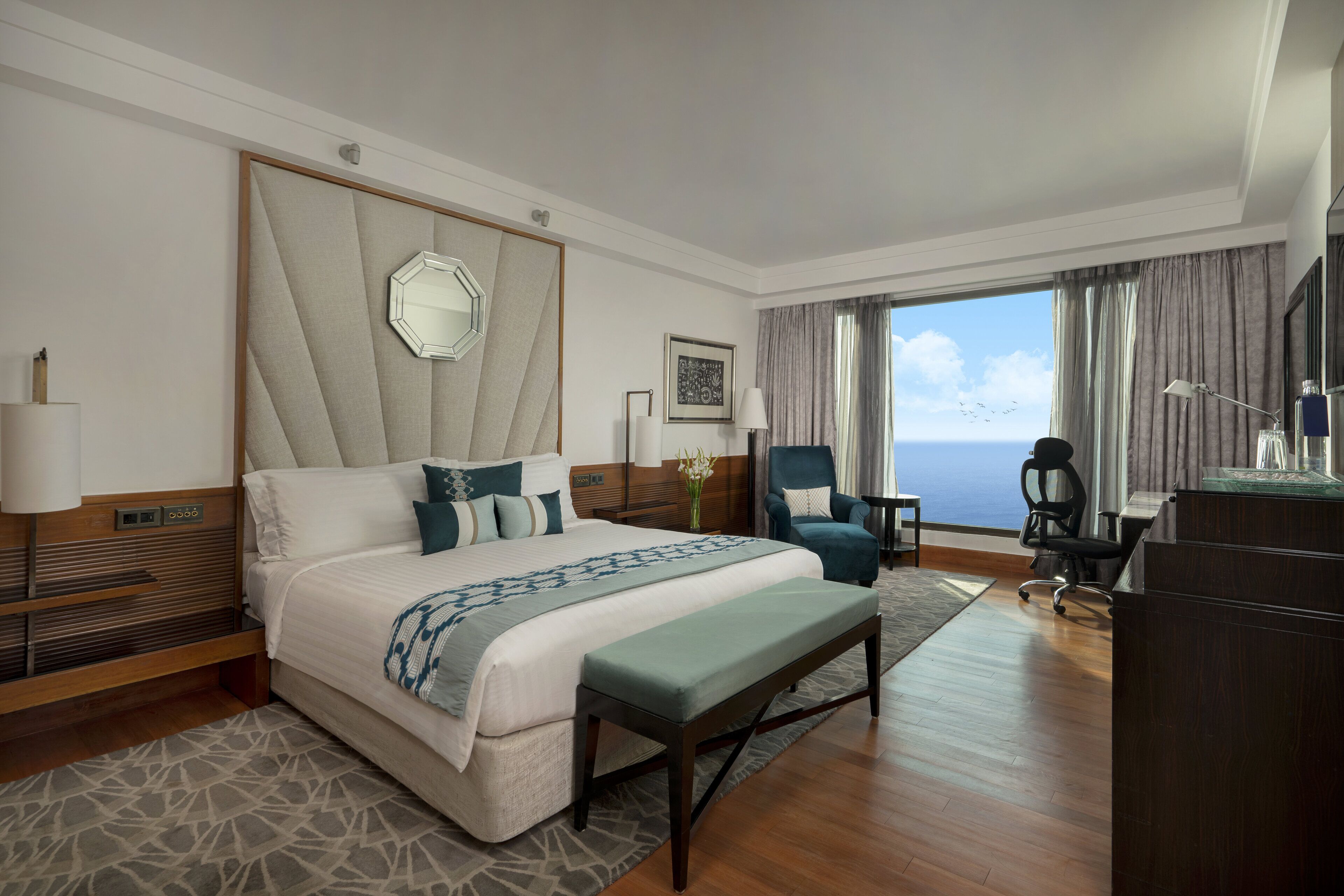 A hotel room with a large bed, a desk, a chair, and a view of the ocean.
