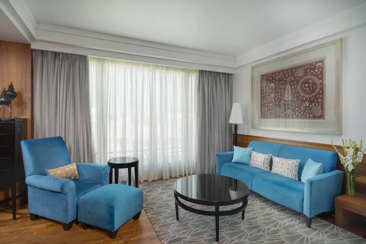 A modern living room with a blue sofa, a matching armchair, a round coffee table, and a large window with sheer curtains.