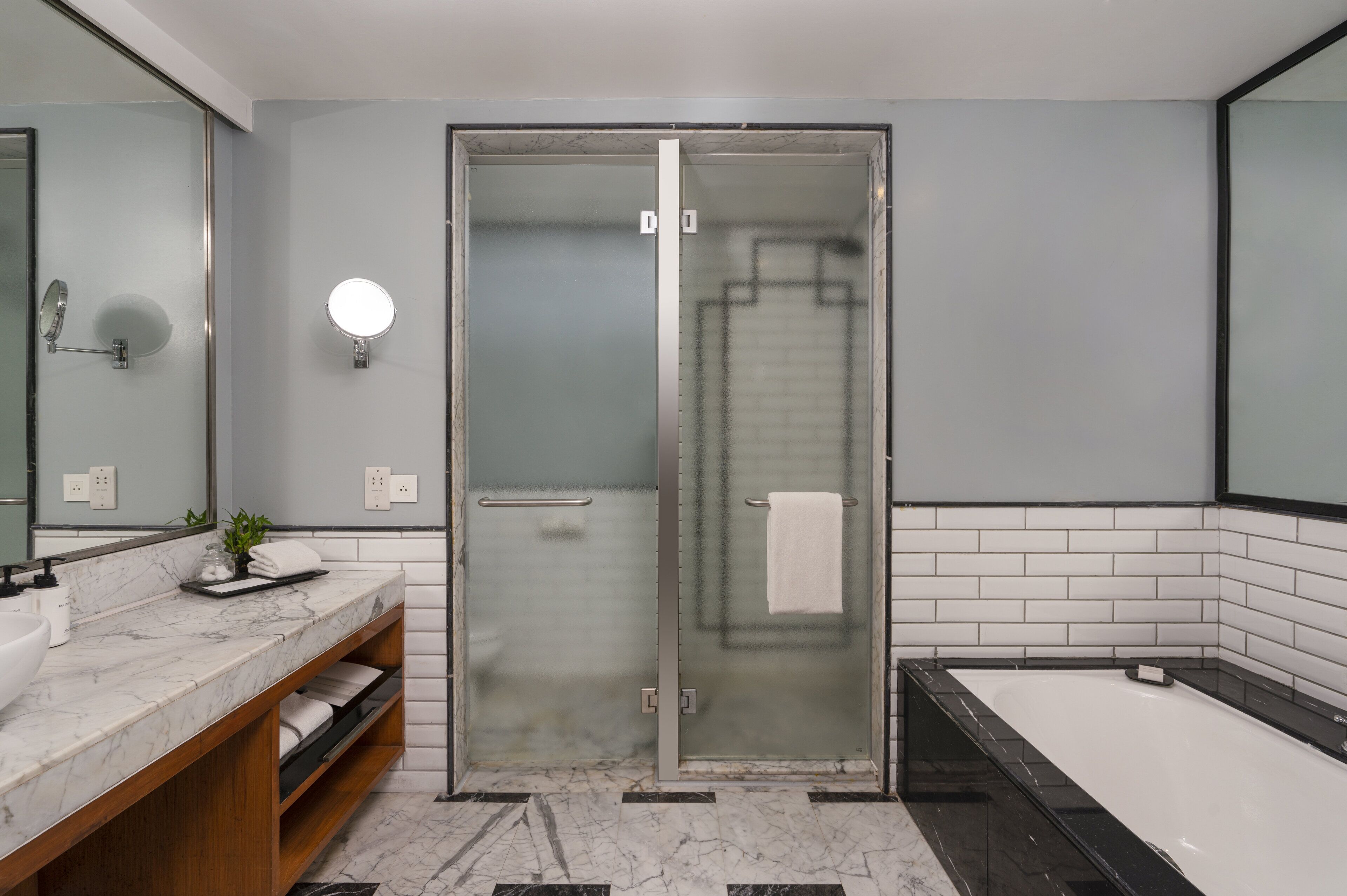 A modern bathroom with a glass-enclosed shower, a large bathtub, and a marble vanity with a sink and mirror.